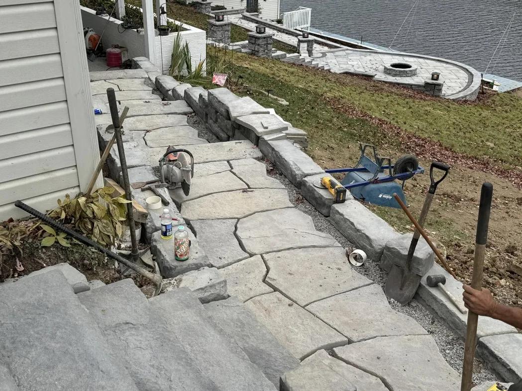 Hardscaping crew setting a flagstone walkway and block wall along a house