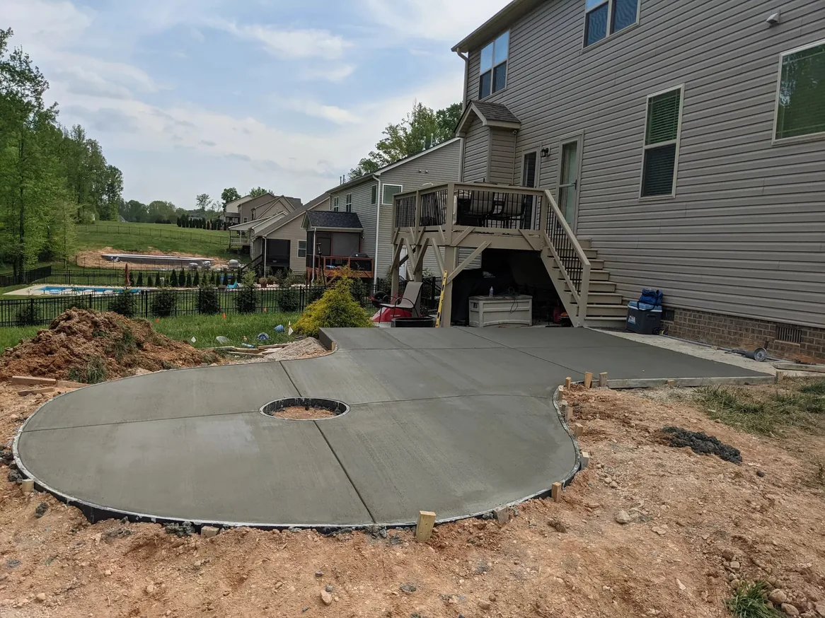 Concrete: a freshly poured broom finished concrete patio with a round fire pit opening behind a house