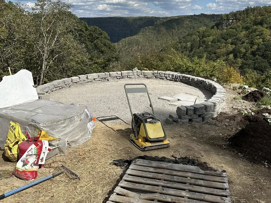 Excavation: a plate compactor on a gravel base inside a curved stone wall on a mountain overlook