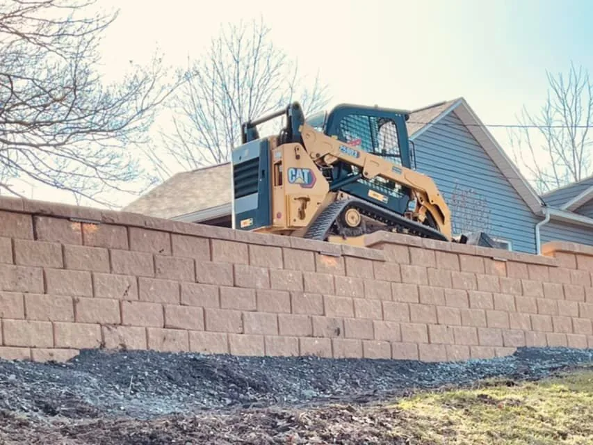 Excavation: a tracked skid steer working on top of a new block retaining wall