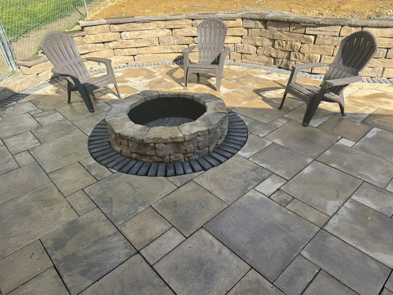 Fire pits: a round block fire pit with Adirondack chairs on a paver patio below a seating wall