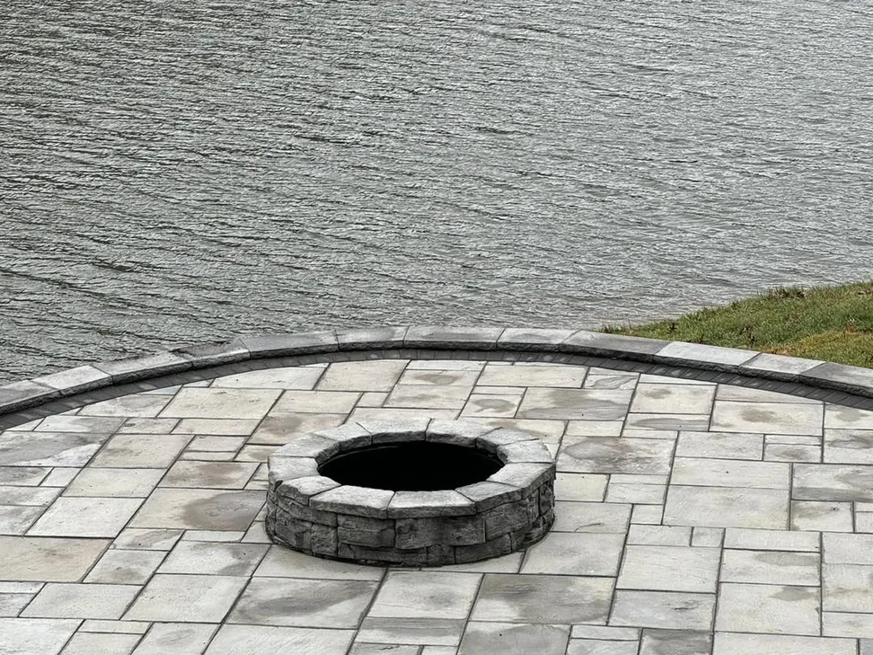 Fire pits: a stone fire pit on a paver patio beside a lake