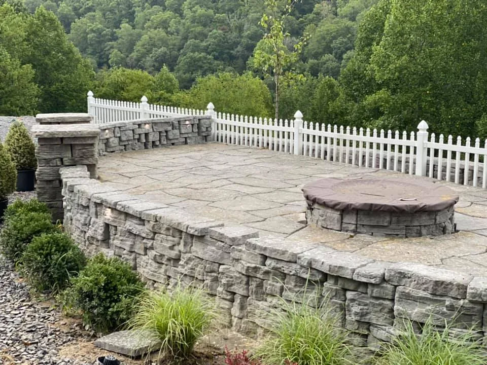 Fire pits: a fire pit and stone seating wall on a patio with a white picket fence and wooded hills