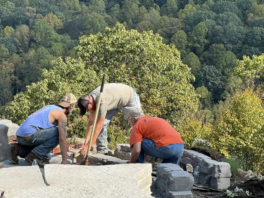 Hardscaping: a crew setting wall block on a patio build with wooded mountains behind