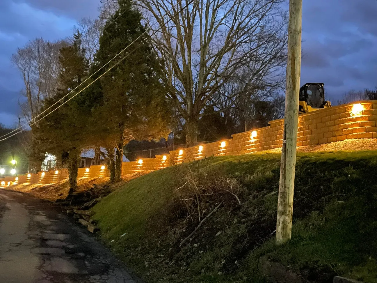 Outdoor lighting: retaining wall cap lights glowing along a slope at dusk