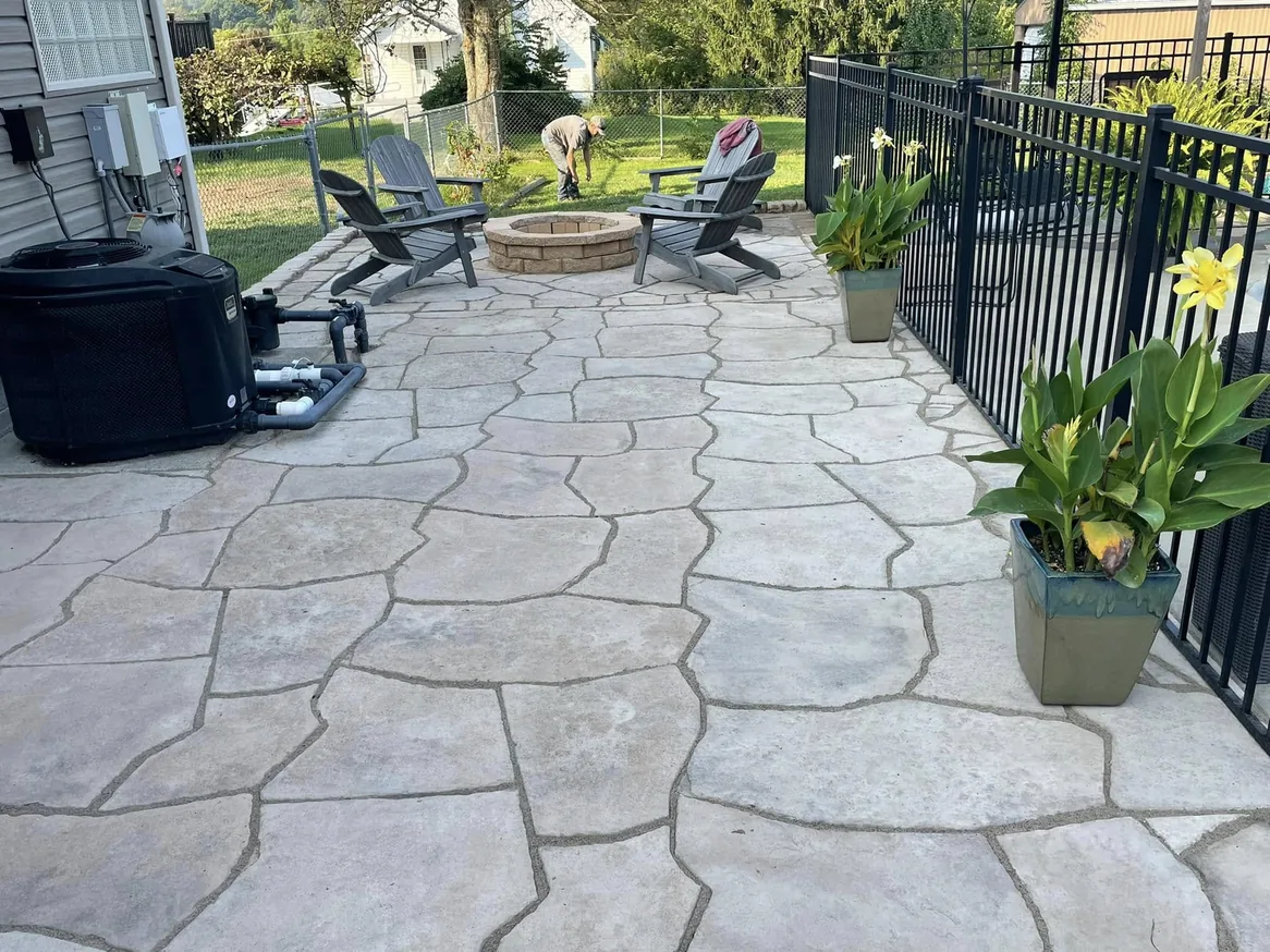 Paver patios: a flagstone pattern paver patio with chairs around a fire pit inside a fenced yard