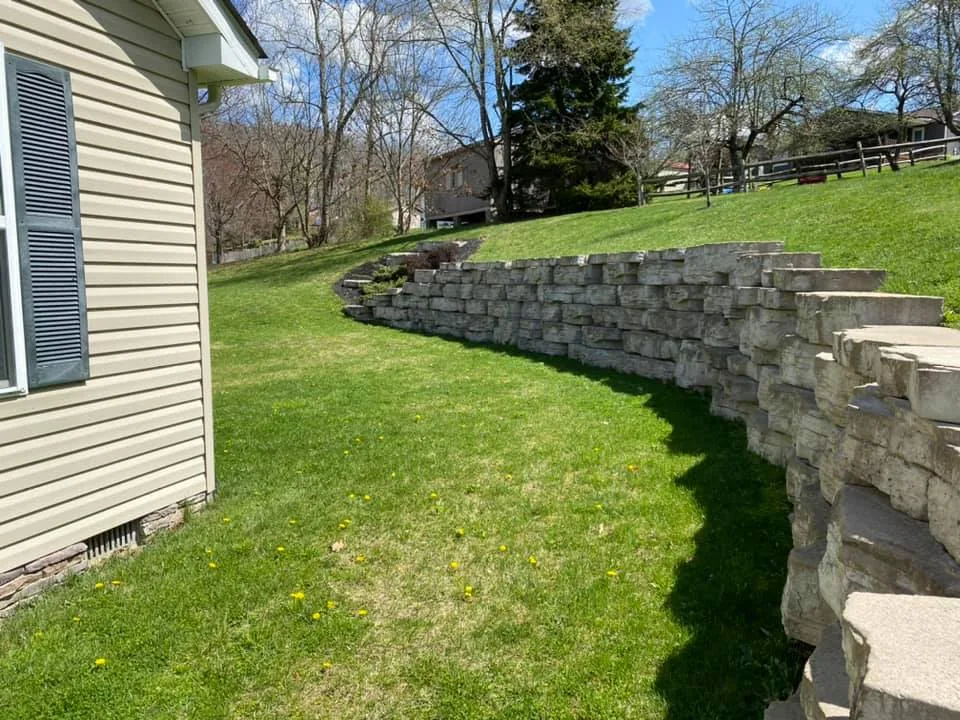 Retaining walls: a long stone block retaining wall following a sloped lawn beside a house