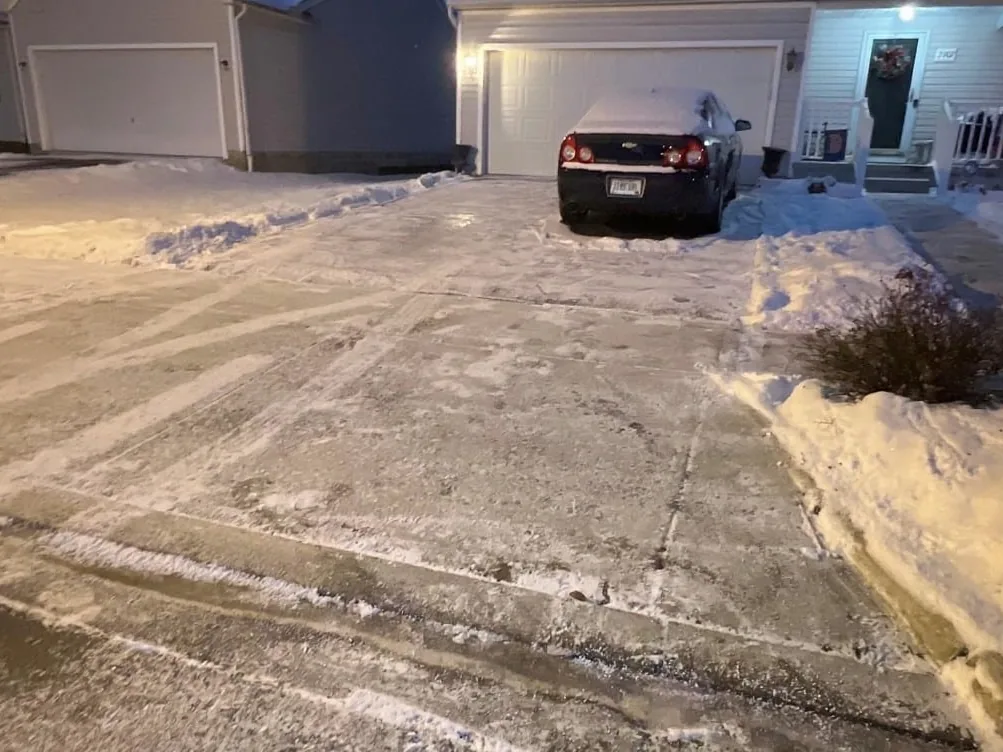 Snow removal: a plowed home driveway at dusk with a car parked before the garage
