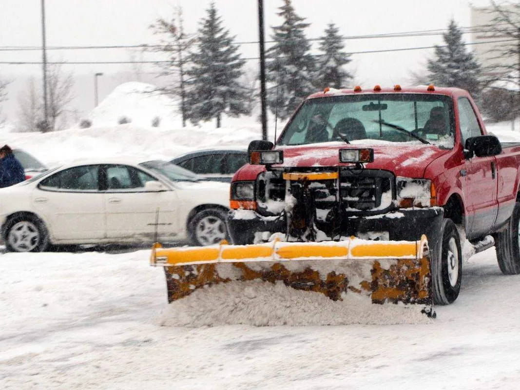 Snow removal: a pickup truck with a straight plow blade clearing snow from a parking lot